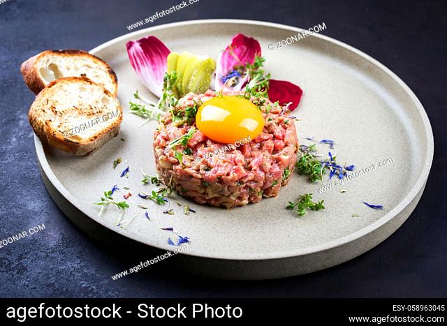 Gourmet tartar raw from beef fillet with yellow of the egg grilled and baguette as closeup on modern design dish