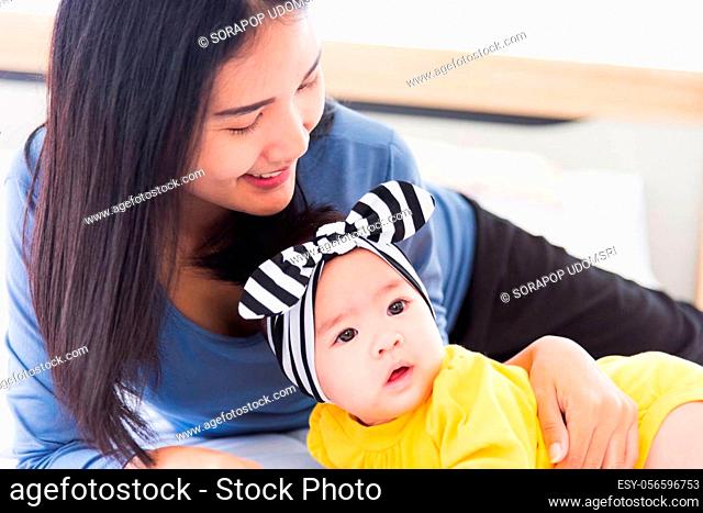 Portrait of beautiful young Asian mother playing and smiling together with his newborn little baby at home, Parent mom and little kid relaxing in the bedroom
