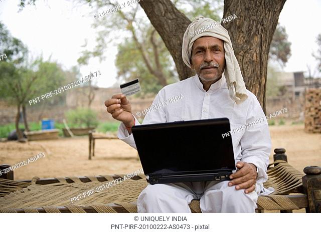 Farmer holding a credit card and using a laptop, Hasanpur, Haryana, India