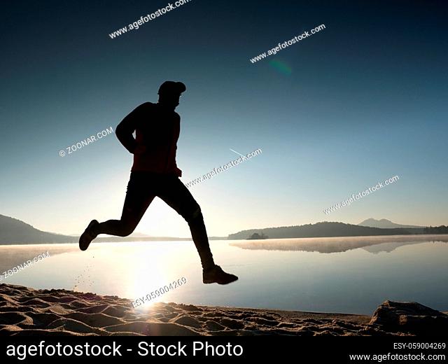 Boy running at the beach during sunrise with reflection. Morning bay beach with clear sky. Lens reflections and flare