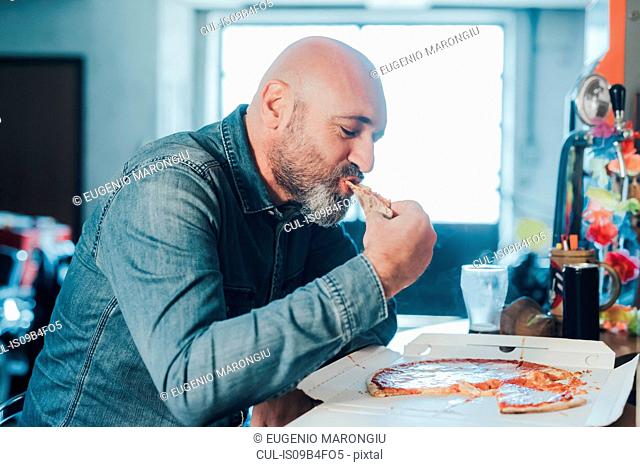 Mature man, sitting at table, eating takeaway pizza