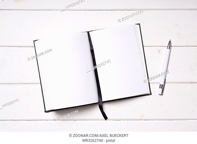 open notebook with blank pages and pen on white wooden desk