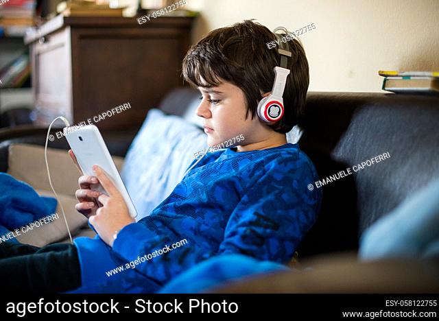 boy listens to music from tablet sitting in house-boy watches video on smartphone with headphones