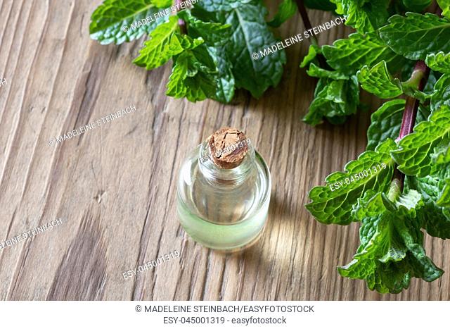 A bottle of essential oil with fresh peppermint leaves on a wooden background