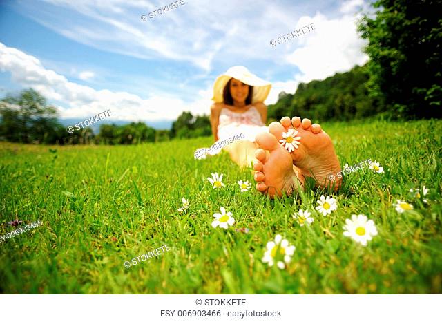 a smiling young woman is lying on a green lawn, with a daisy between her toes shallow deep of field selective focus DOF