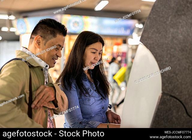 Smiling man with mature woman using ATM machine