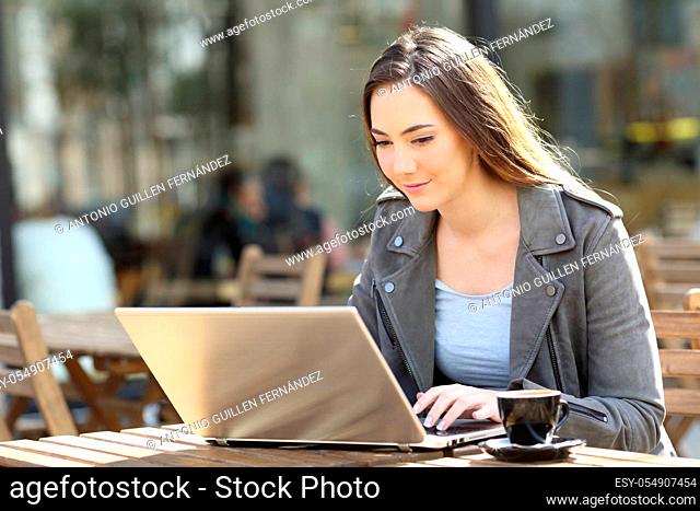 Young woman using her laptop sitting on a restaurant terrace a sunny day