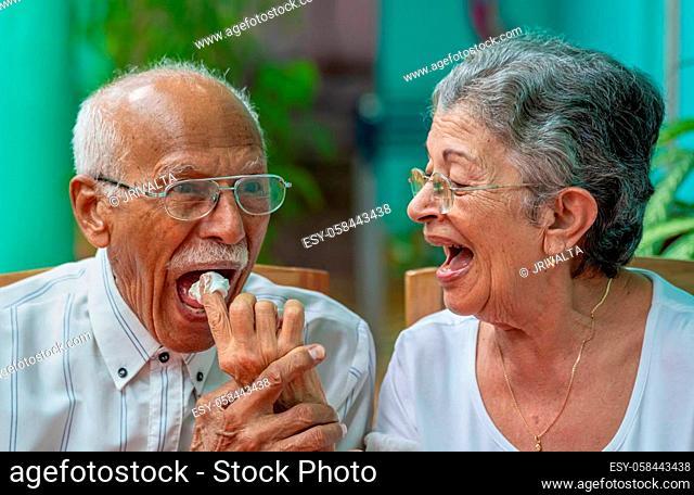 Elderly couple looking at each other smilingly. The old woman giving meringue cake to the old man