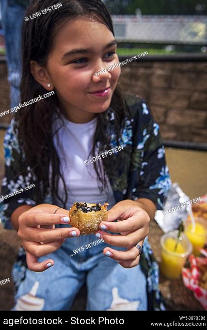 A hispanic teenage girl eats a deep-fried Oreo cookie at the county fair in Arlington, Virginia