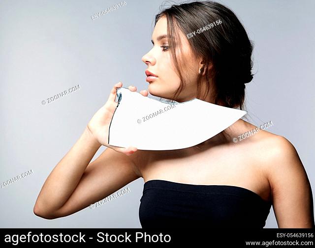 Girl with a shard of the mirror. Female with mirror shard in hand posing on gray background