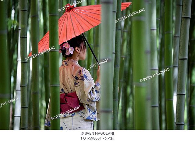 A woman wearing a kimono and standing in a bamboo grove