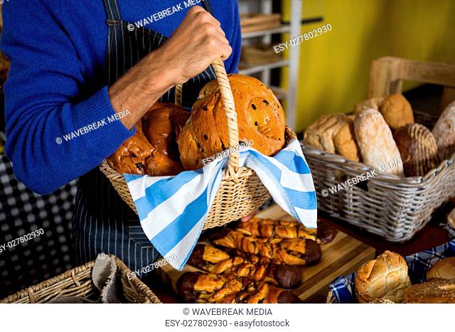 Mid section of staff holding wicker basket of breads at counter