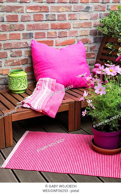 Balcony with bench, pink cushion, blanket, lantern, mat and various potted plants