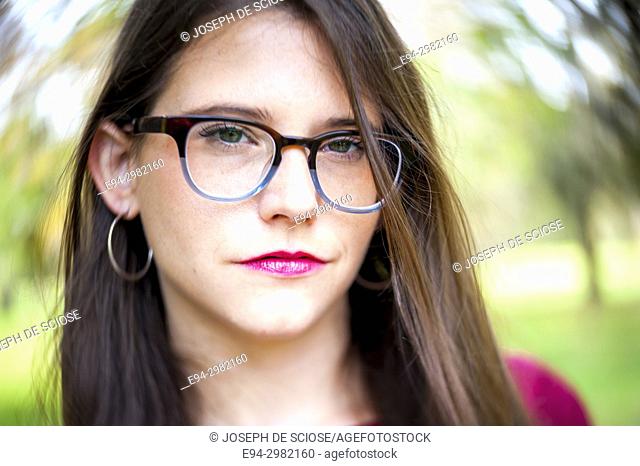A casual portrait of a 26 year old woman with long brown hair and big glasses, outdoors
