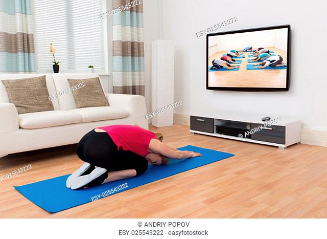 Young Woman In Sportswear Doing Yoga In Front Of Television At Home