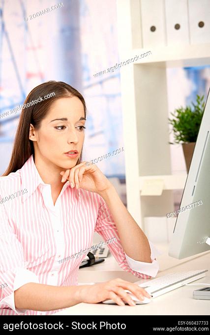 Young assistant girl sitting at desk in office concentrating on computer work