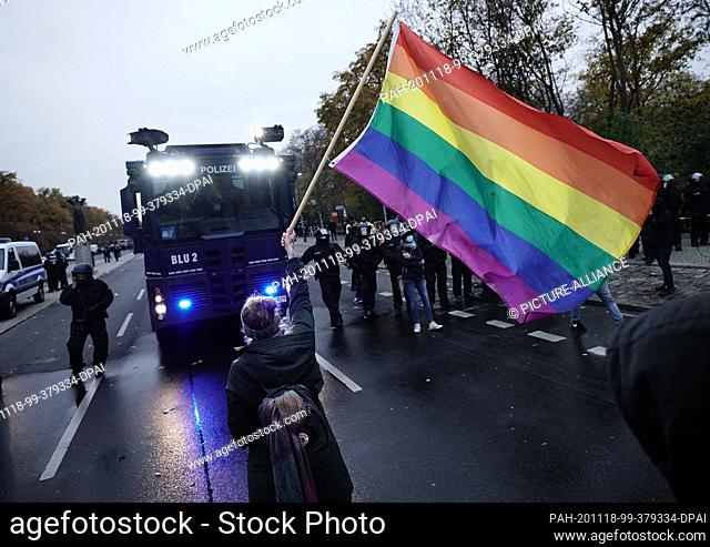 18 November 2020, Berlin: A participant in a demonstration against the Corona restrictions of the German government stands with a rainbow flag in front of a...