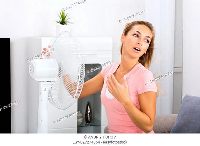 Young Woman Cooling Herself During Hot Weather In Front Of Fan At Home