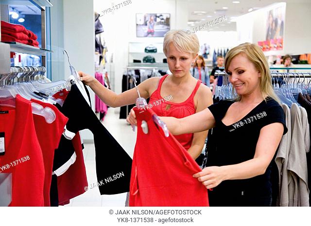 Young women shopping and comparing different clothes in store