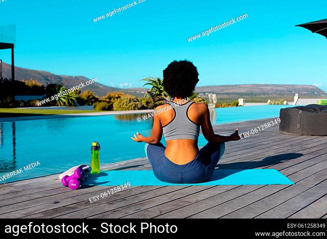 Rear view of african american woman practicing yoga and meditating near the pool