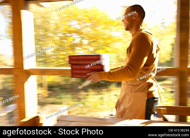 Dueño de pizzería masculino llevando cajas de pizza a lo largo de la ventana soleada de otoño