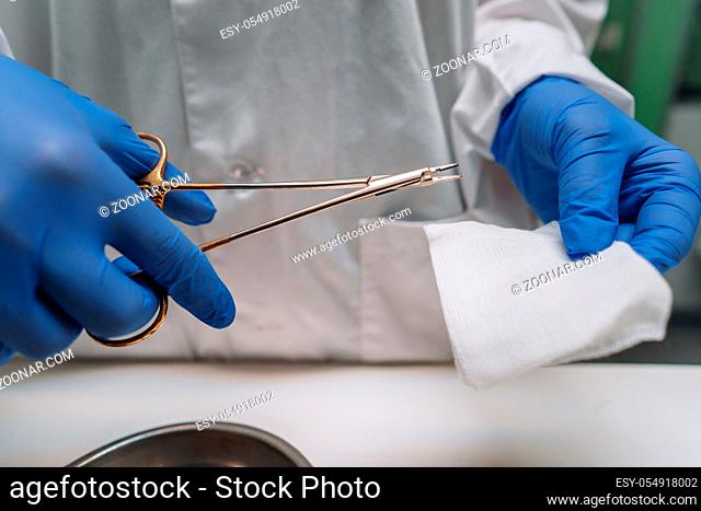 Women's hands in rubber gloves hold a clip and gauze, close angle