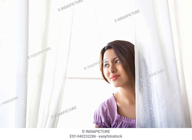 Young woman behind curtains