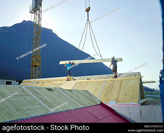 Carpenters installing roof with help of crane at construction site