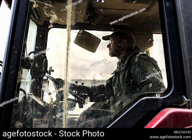 Side view of farmer sitting in the cabin of a tractor