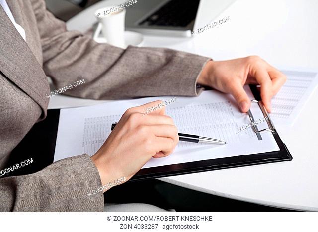 Hand einer Geschäftsfrau am Schreibtisch mit Stift und Klemmbrett