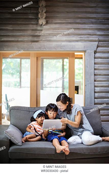 Woman, boy and young girl sitting on a grey sofa, looking at digital tablet