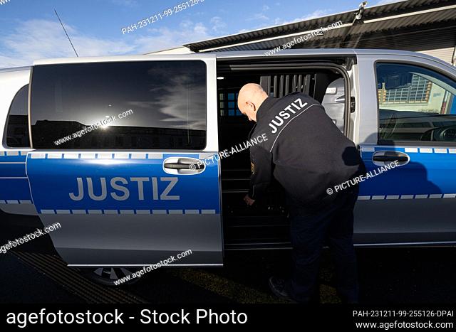 11 December 2023, Saxony, Dresden: A prison officer closes a gate in a fully electric prisoner transport vehicle during the handover of the vehicles to the...