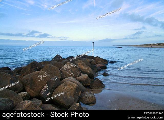 Stone groyne juts out into the water off the coast in Denmark. Sunny day. Landscape photo by the sea