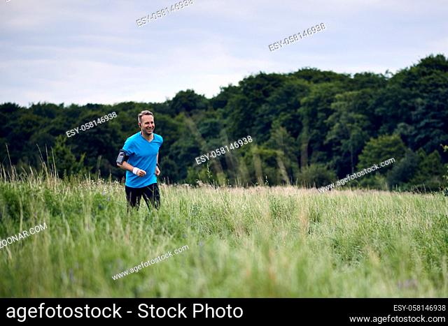 Fit muscular man jogging on a rural trail through grassland wearing sportswear in an active lifestyle concept