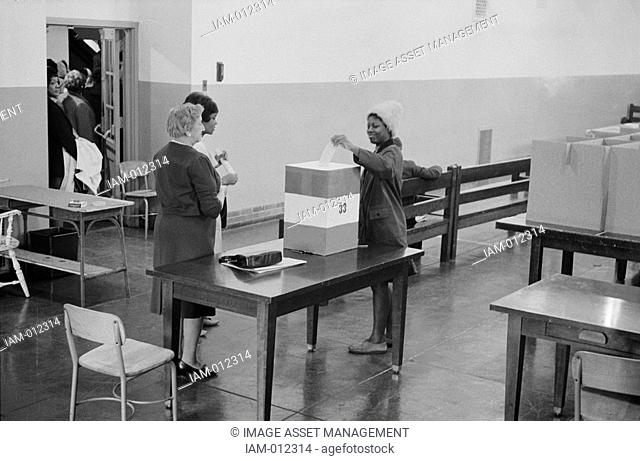 Young African American woman casting her vote in a ballot box at voting station in the Cardoza High School building, Washington. DC, 3 May 1964
