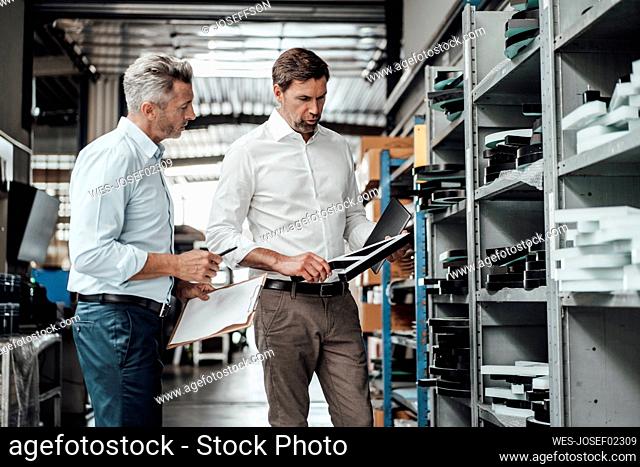 Businessmen discussing over equipment while standing by rack in factory