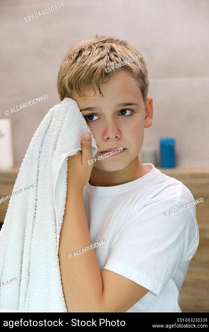 Reflection of a schoolboy wiping his face with a towel after washing in the bathroom. Morning hygiene procedures