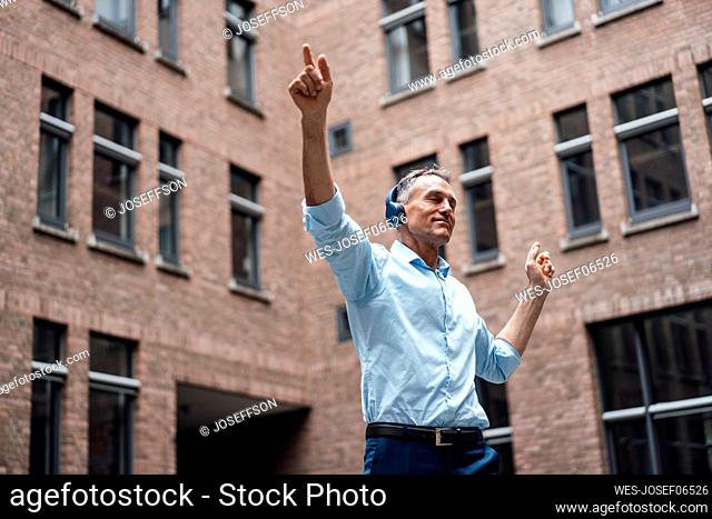 Businessman with eyes closed enjoying music and dancing in front of office building
