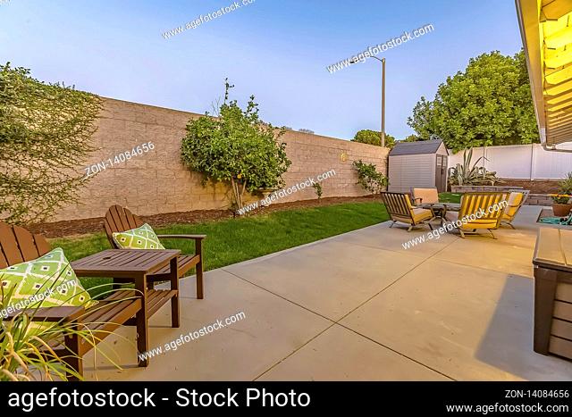 Spacious patio at the backyard of a home with a seating and dining area. A small shed is at the corner of the yard enclosed inside a concrete and wooden fence