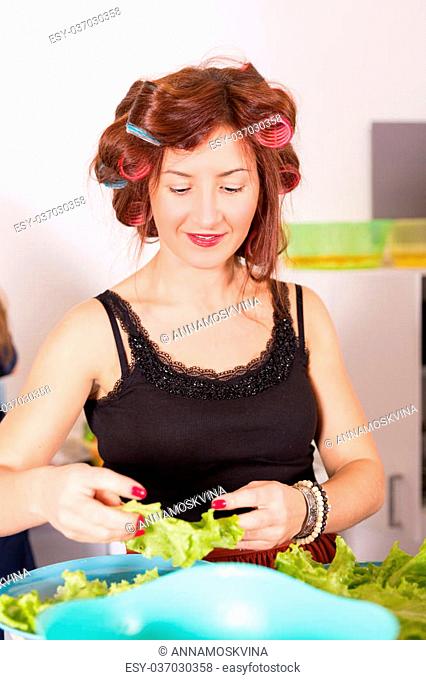 Young pretty woman housewife cooking with curlers on hair