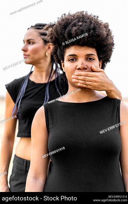 Woman's hand covering mouth of another woman