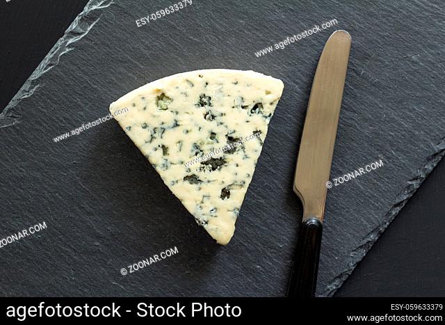 Blue cheese triangle with knife isolated on black slate cheese board - Roquefort type cheese top view photograph