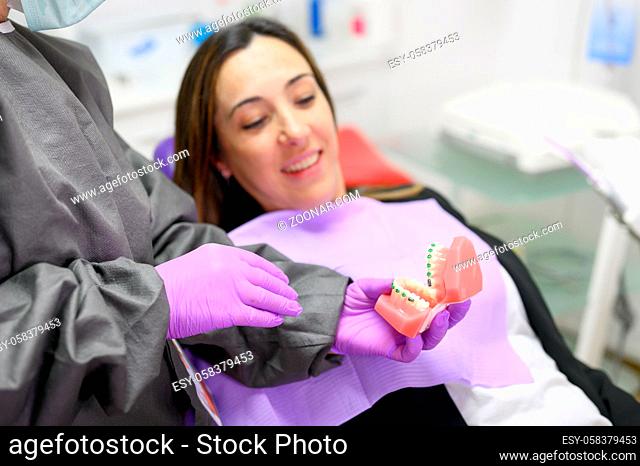 Dentist showing to patient an orthodontics dental model, explaining to patient the orthodontics treatment in dental clinic. High quality photo