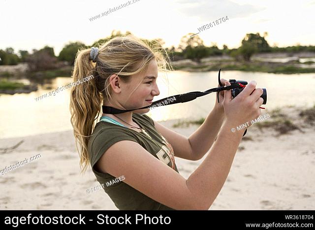 A twelve year old girl taking pictures on vacation in Botswana at sunset, on the banks of the Zambezi River