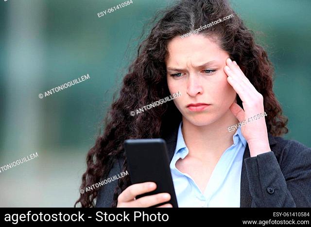 Sad businesswoman checking bad news on smart phone in the street