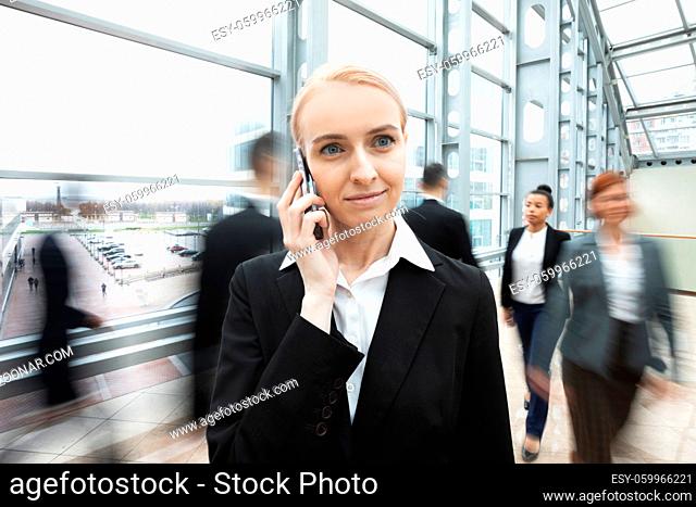 Business woman talking on phone standing in a crowd of walking people