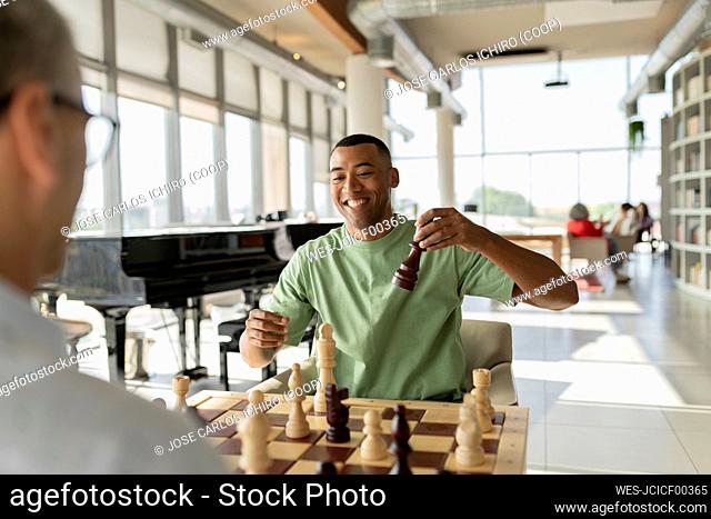 Smiling businessman playing chess with mature colleague in office