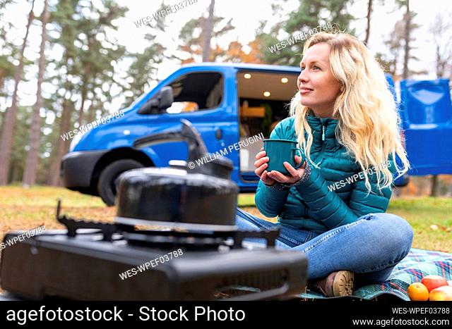 Blond woman holding tea cup while day dreaming during camping at Cannock Chase