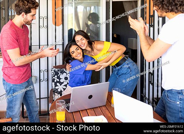 Young men clapping while looking at smiling beautiful women embracing at back yard