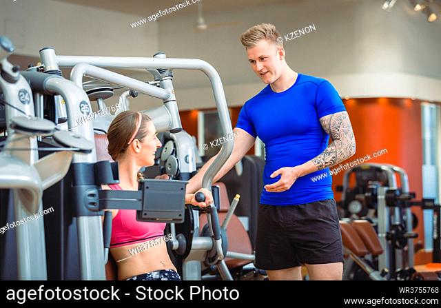 Handsome and experienced personal trainer guiding a beautiful woman while exercising for pectoral muscles and shoulders at a modern fitness club